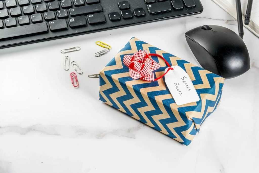 Office Christmas celebration concept, the idea of sharing gifts secret Santa. Keyboard, mouse, notebook, pens, pencils, Christmas gift. White office table, copy space (Office Christmas celebration concept, the idea of sharing gifts secret Santa. Keybo